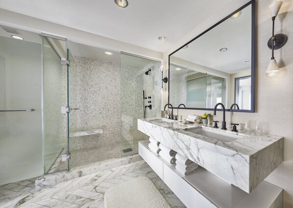 Un baño moderno con ducha de vidrio, un espejo grande y tocador de mármol.