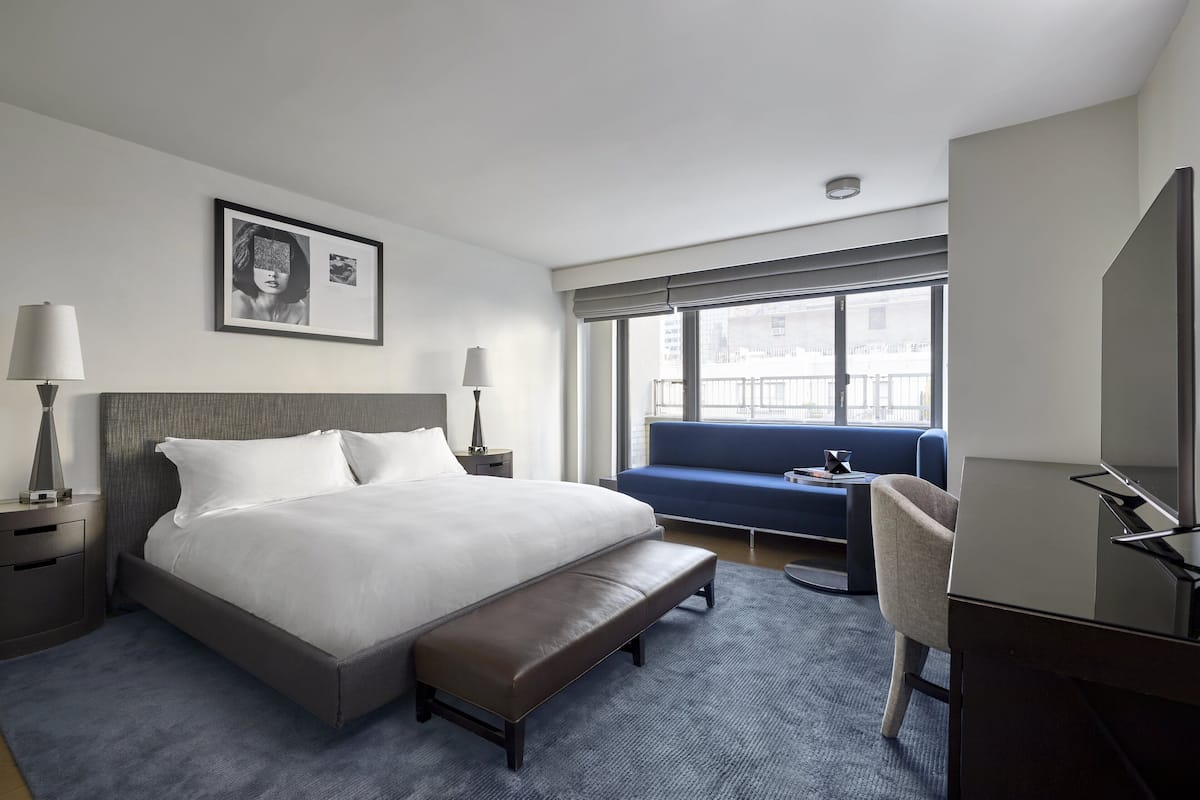 A modern hotel room with a large bed, a bench, a desk, and a sofa.