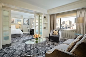 A hotel room with a bed, a sofa, a glass coffee table, a desk, and a view of the city. - Loews Regency New York Hotel (New York)