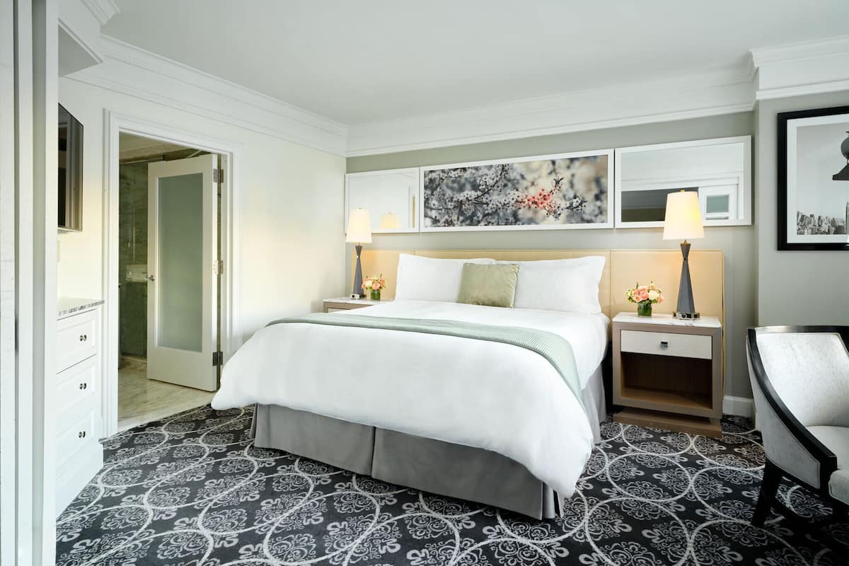 A hotel room with a large bed, two bedside tables, a chair, and a door leading to a bathroom.