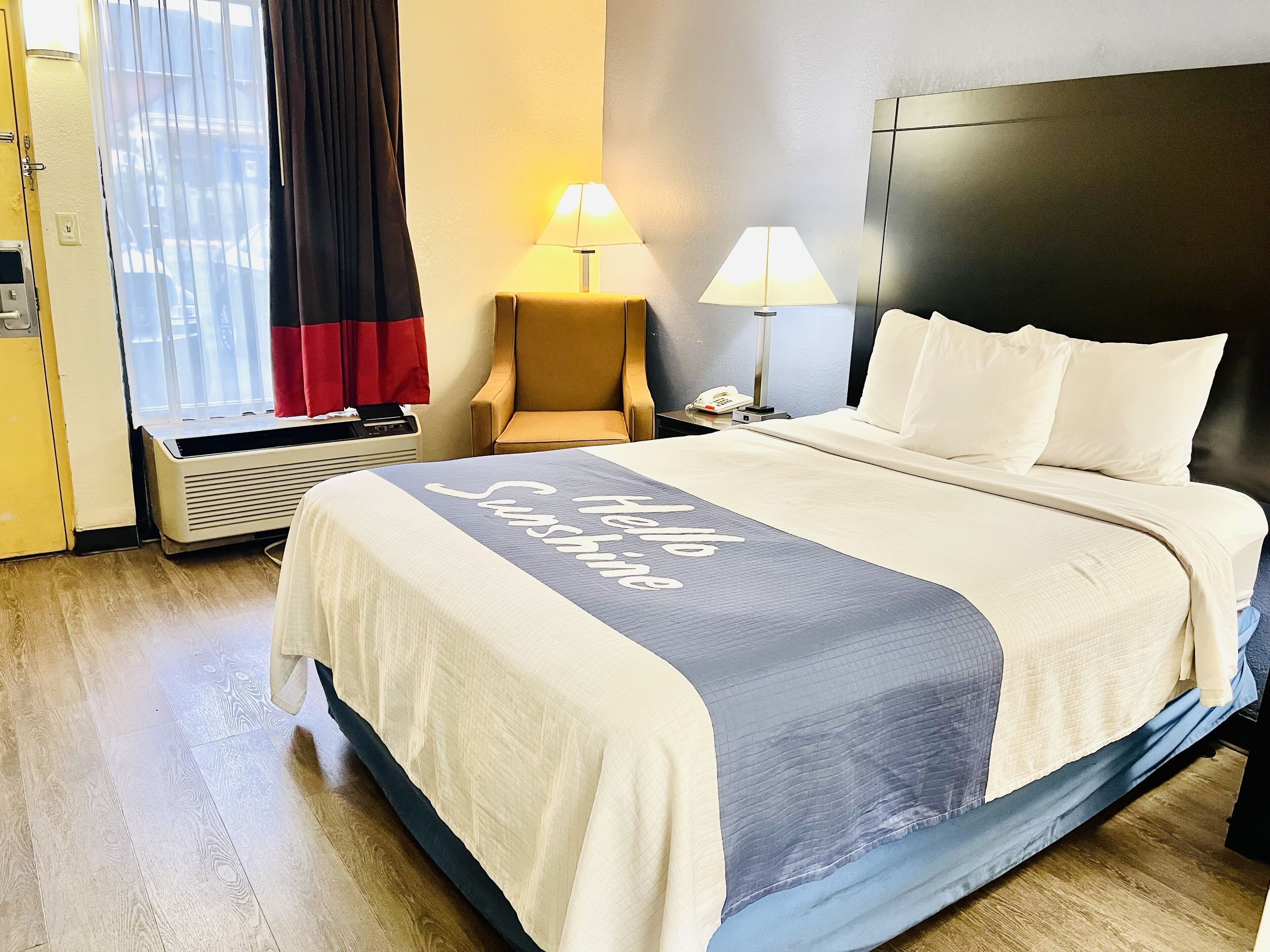 A hotel room with a bed, two bedside lamps, a chair, a telephone, and a window with curtains.