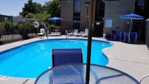 A clear blue swimming pool with lounge chairs and umbrellas, surrounded by a fence and a building with a brick facade. - Days Inn by Wyndham Easley/Greenville/Clemson Area (Easley)