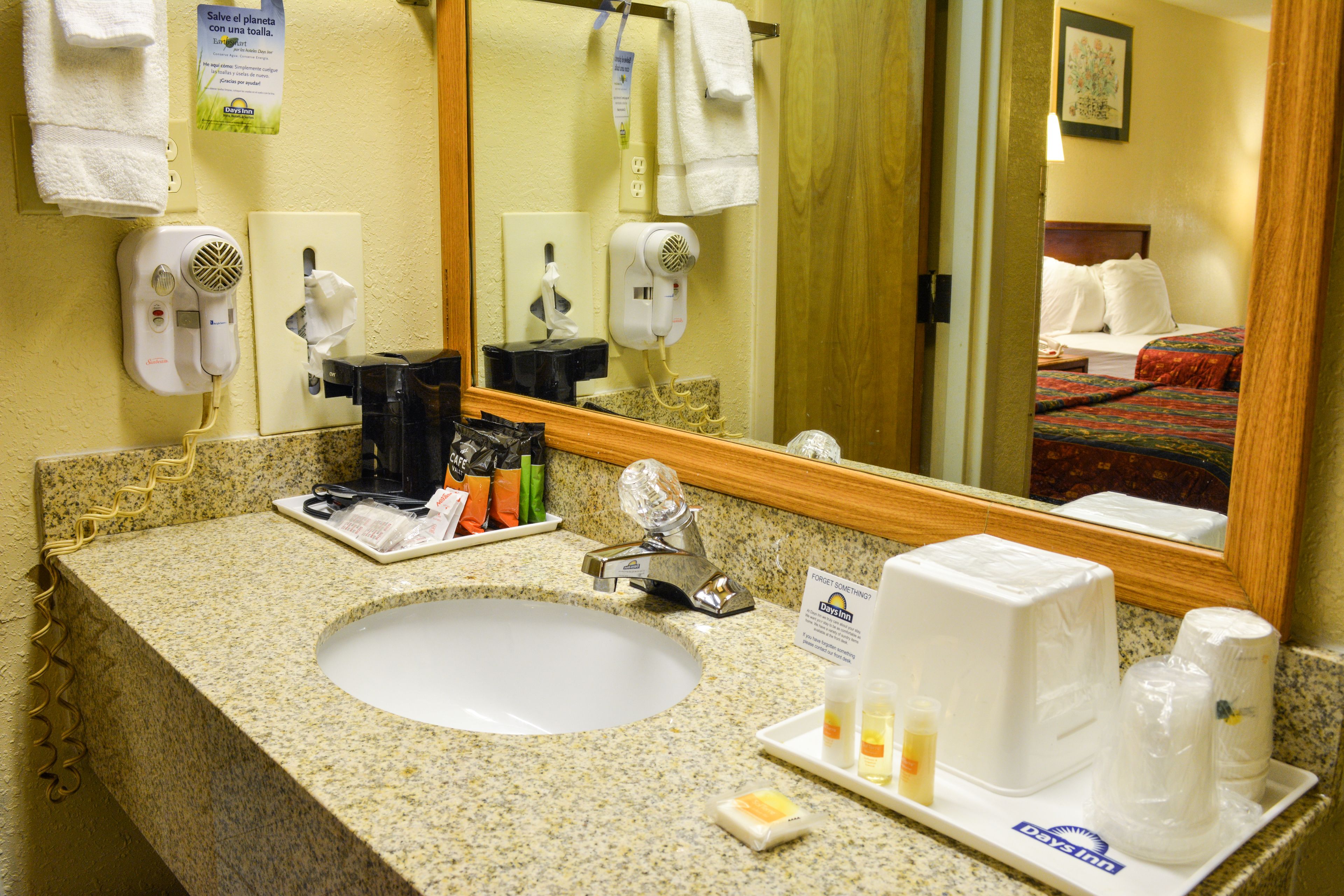 A hotel bathroom with a granite countertop sink, a mirror, a hairdryer, and a towel rack.