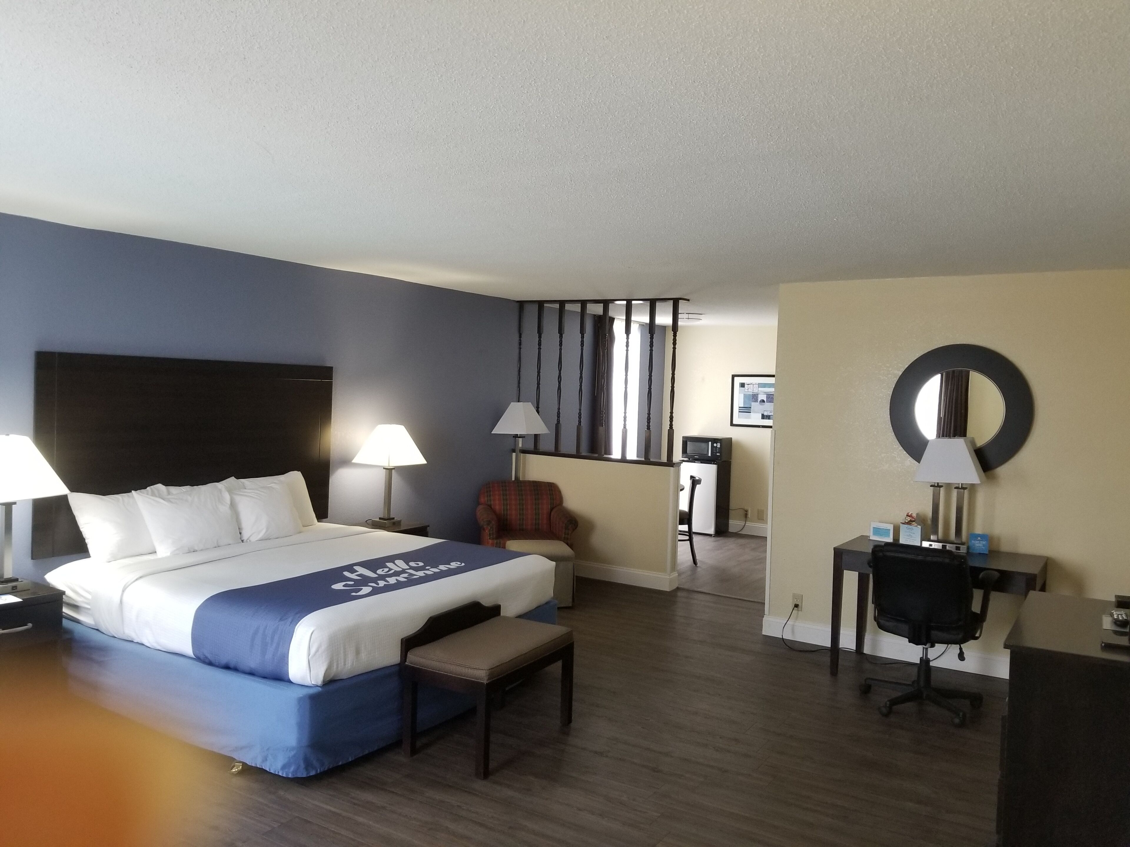 A hotel room with a bed, two bedside lamps, a chair, a desk with a chair, a small TV, and a mirror on the wall.