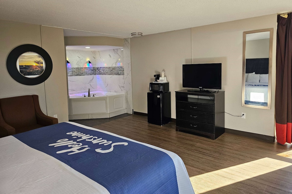 A hotel room with a bed, a TV, a microwave, and a bathroom with a jacuzzi.
