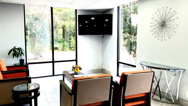 A modern waiting area with two chairs, a small table, a potted plant, and a wall-mounted clock. - Days Inn by Wyndham Easley/Greenville/Clemson Area (Easley)