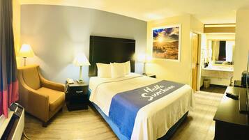 A hotel room with a bed, a chair, a desk with a computer, a lamp, and a painting on the wall.