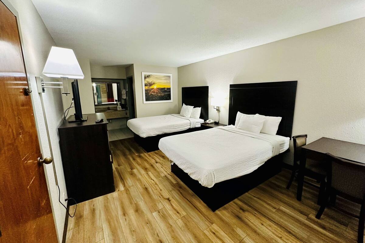 A hotel room with two beds, a desk, a chair, a wardrobe, and a painting on the wall.