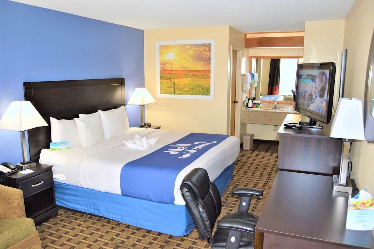 A hotel room with a bed, a desk, a chair, a television, and a bathroom mirror.