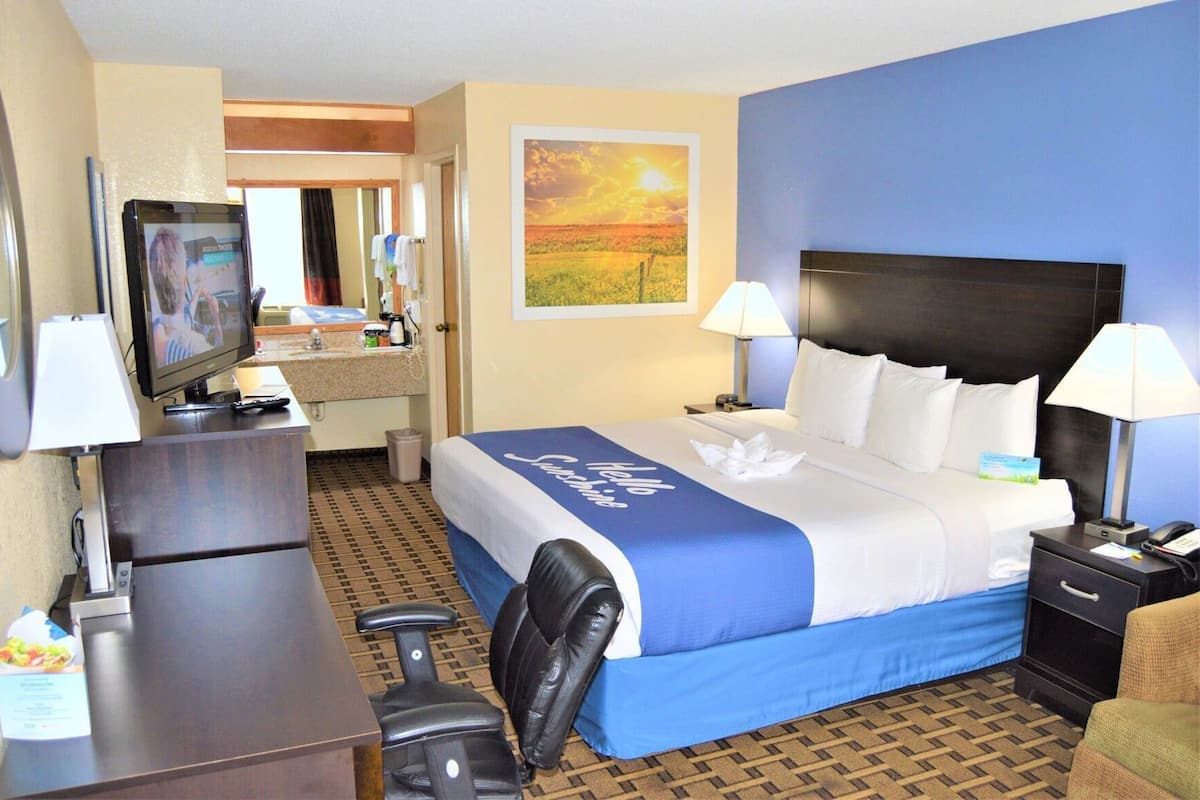 A hotel room with a bed, desk, chair, TV, and a painting on the wall.