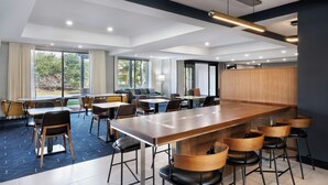 A modern hotel dining area with a long communal table, multiple chairs, and a bar counter.