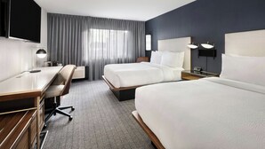 A hotel room with two beds, a desk, a chair, a flat-screen TV, and a large window with curtains.