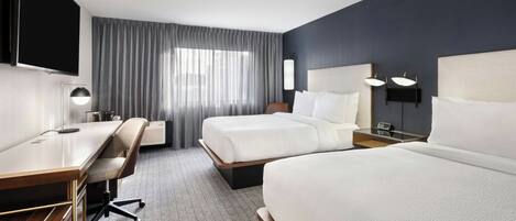 A hotel room with two beds, a desk, a chair, a flat-screen TV, and a large window with curtains.