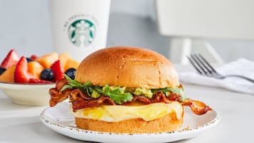 Een belegd boterham op een bord, met een Starbucks-beker op de achtergrond.