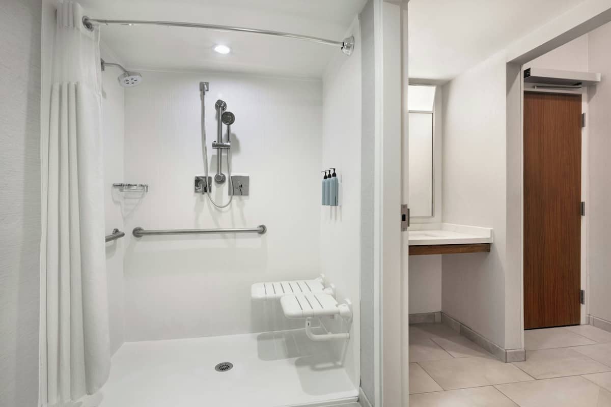 A modern bathroom with a walk-in shower, grab bars, a bench, and a vanity with a mirror.