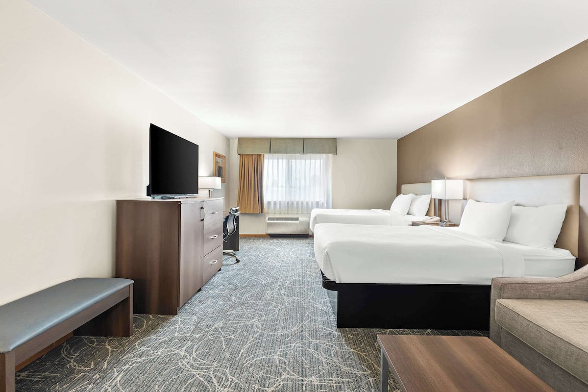 A hotel room with a large bed, a desk with a flat-screen TV, a bench, and a sofa.