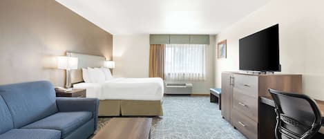 A hotel room with a bed, a sofa, a desk, a TV, and a dresser.