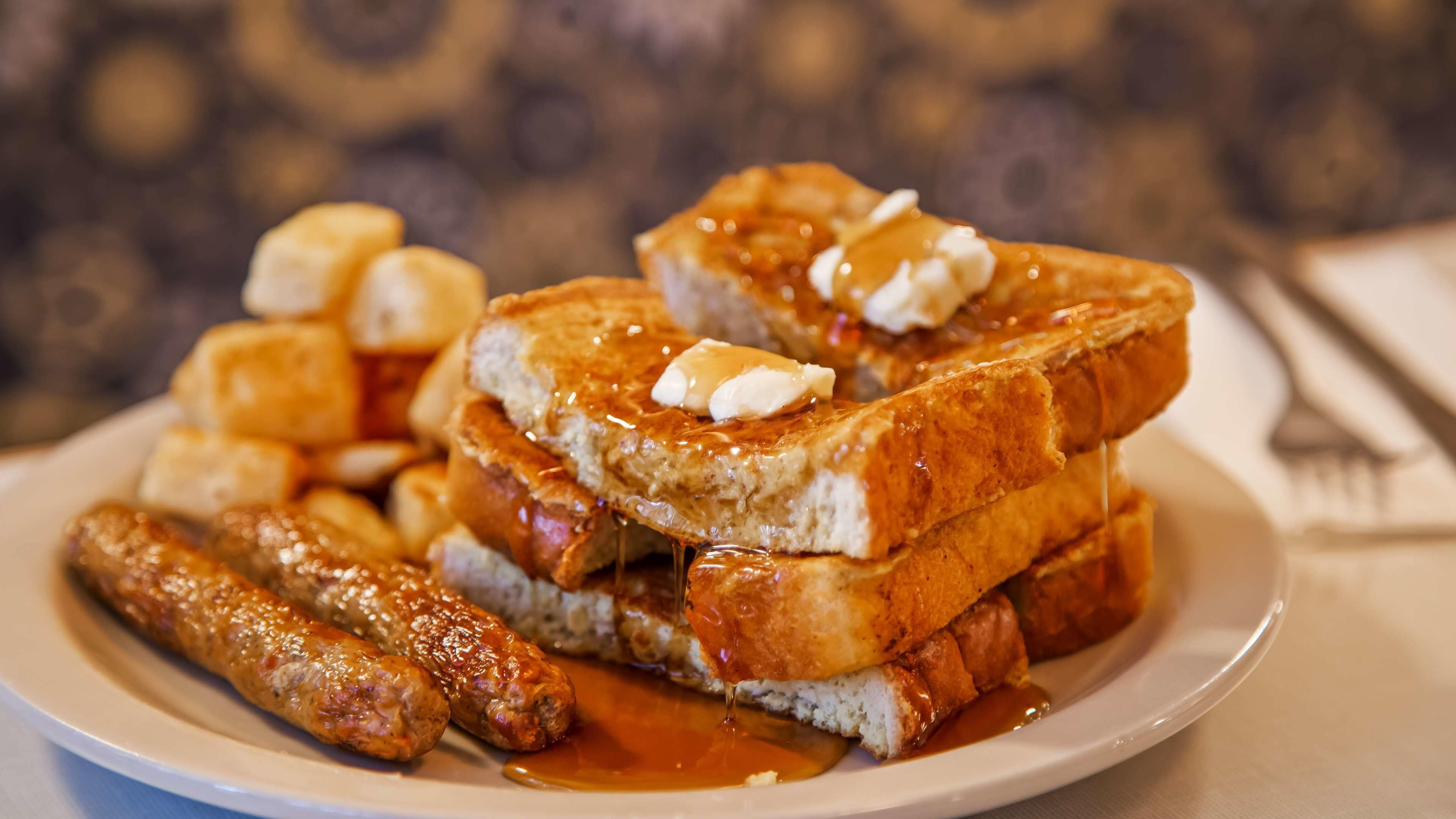 A plate of French toast with bananas and syrup, accompanied by sausages.