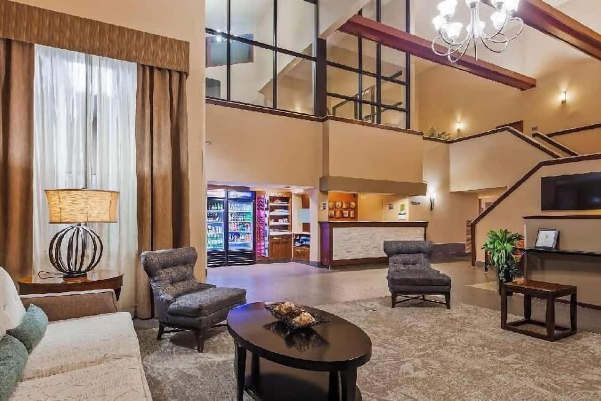 A spacious lobby with a sofa, armchairs, a coffee table, a reception desk, and a staircase.