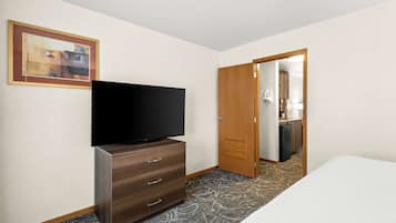 Ein Hotelzimmer mit einem Flachbildfernseher auf einer Kommode, einem Bett, einer Tür zu einem Badezimmer und einem gerahmten Bild an der Wand.