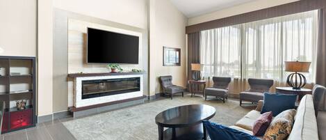 A modern living room with a flat-screen TV, fireplace, comfortable seating, and large windows.