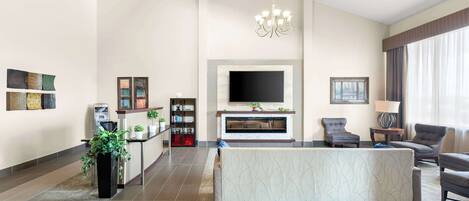 A spacious living room with a large sofa, a fireplace, a television, and a chandelier.