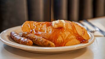 A plate with a croissant, sausage, and a glass of juice.