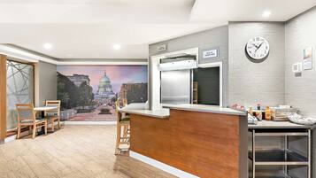 Zona de recepción de hotel con un mostrador de madera, un reloj y un mural de un paisaje urbano.