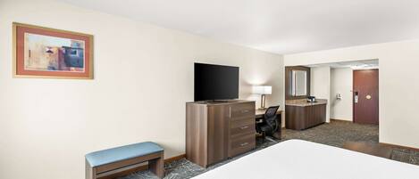 A hotel room with a large bed, a desk with a computer, a television, a bench, and a dresser.