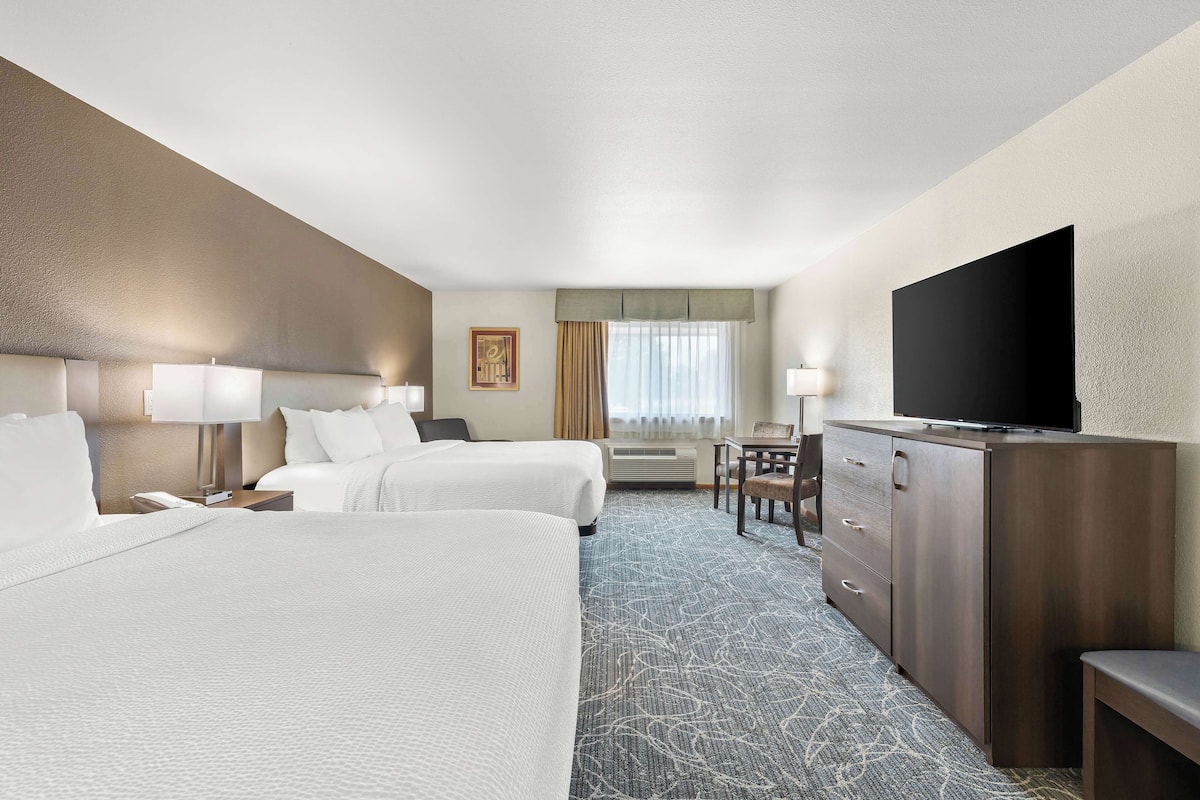 A hotel room with two beds, a desk, a TV, and a dresser.