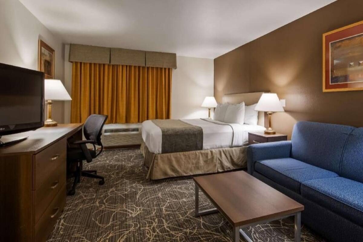 A hotel room with a bed, a blue sofa, a desk with a TV, and a lamp.