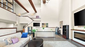 Amplia sala de estar con sofá, mesa de centro y chimenea. Una escalera conduce a un nivel superior, y se observa una zona de cocina al fondo.