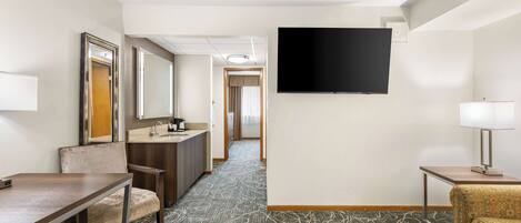 A hotel room with a bed, a desk, a chair, a TV, and a bathroom.