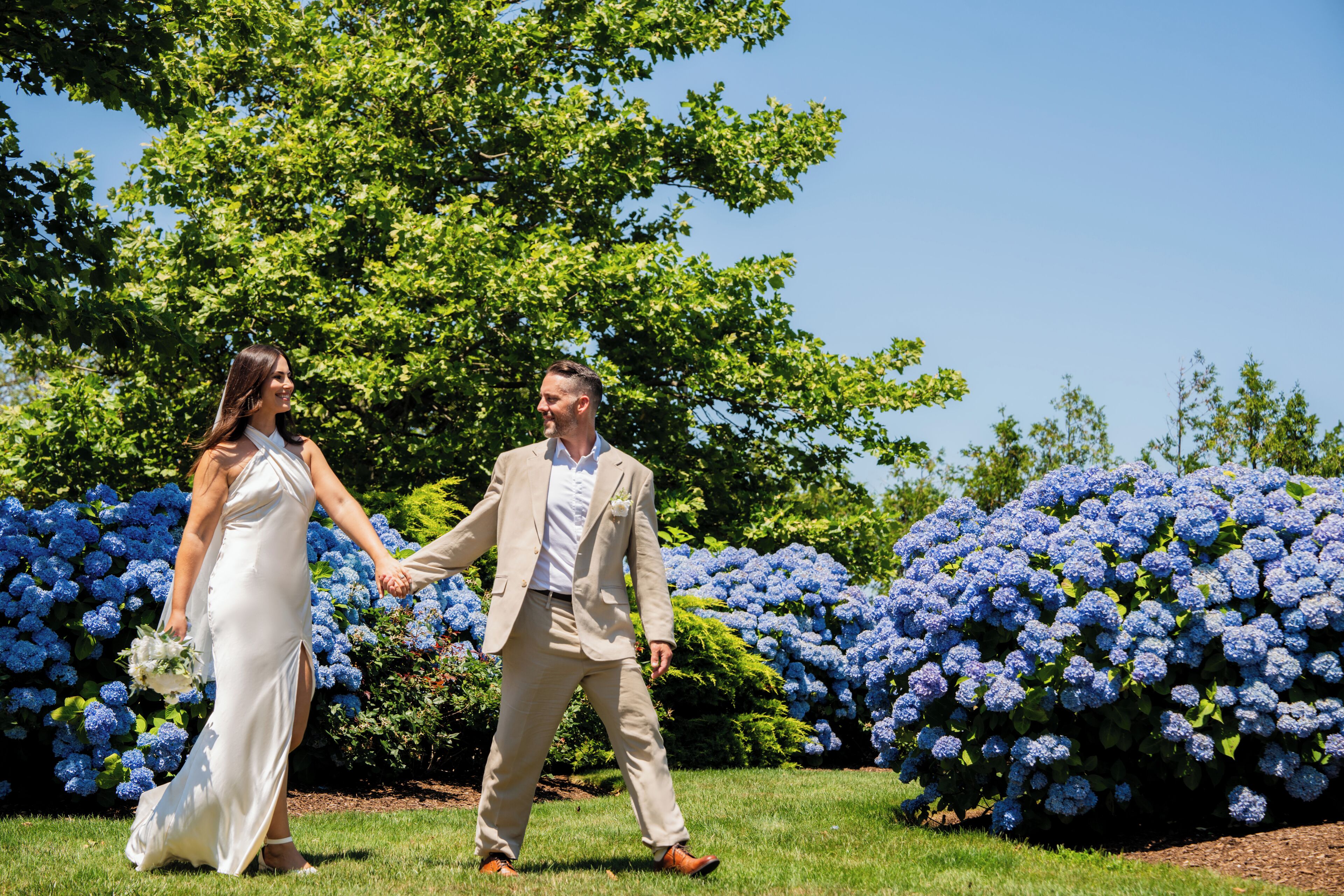 A couple holding hands in a garden with blue hydrangea bushes.