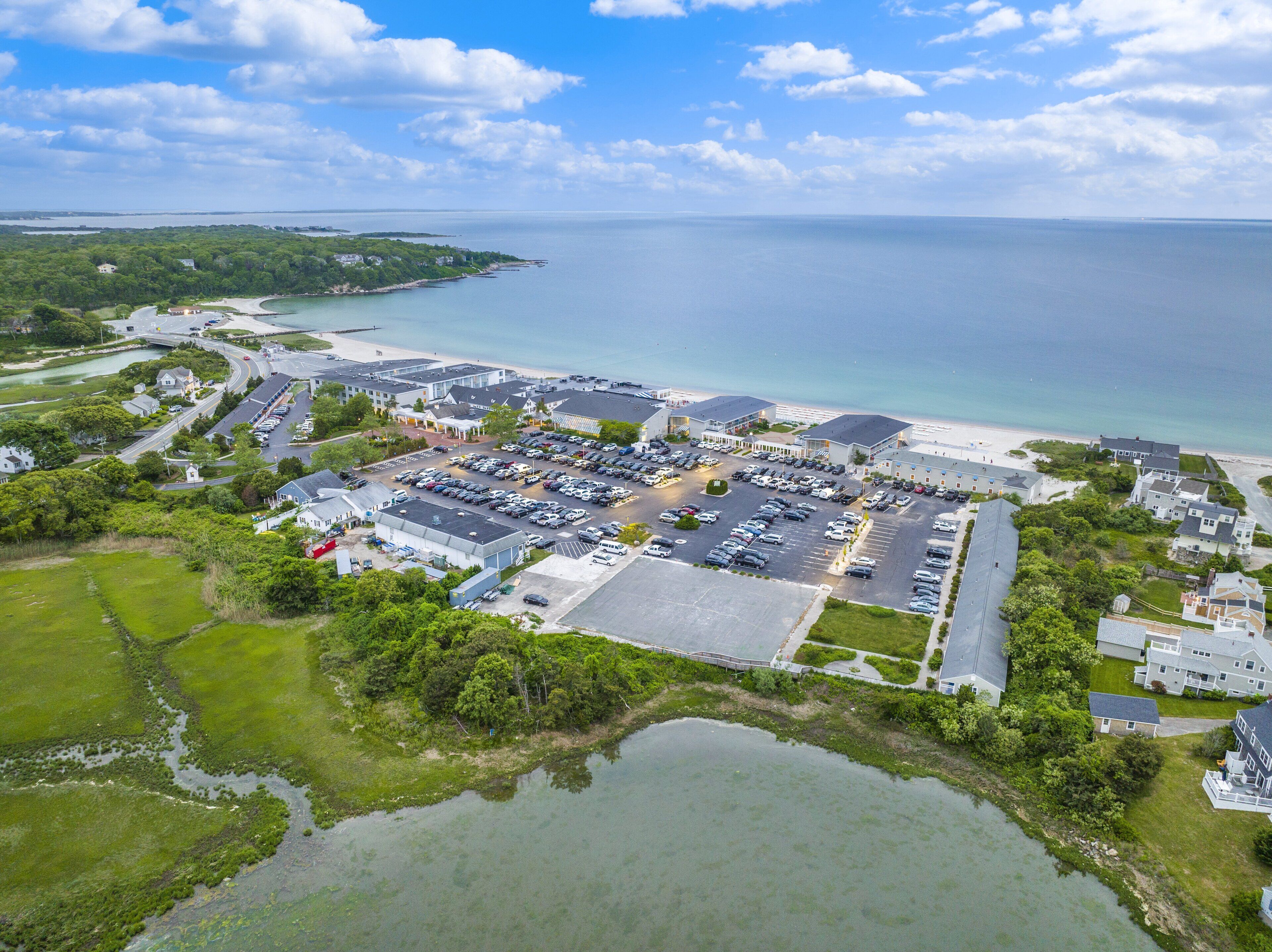 Vue aérienne d’une zone côtière avec un grand parking, des bâtiments et une plage.