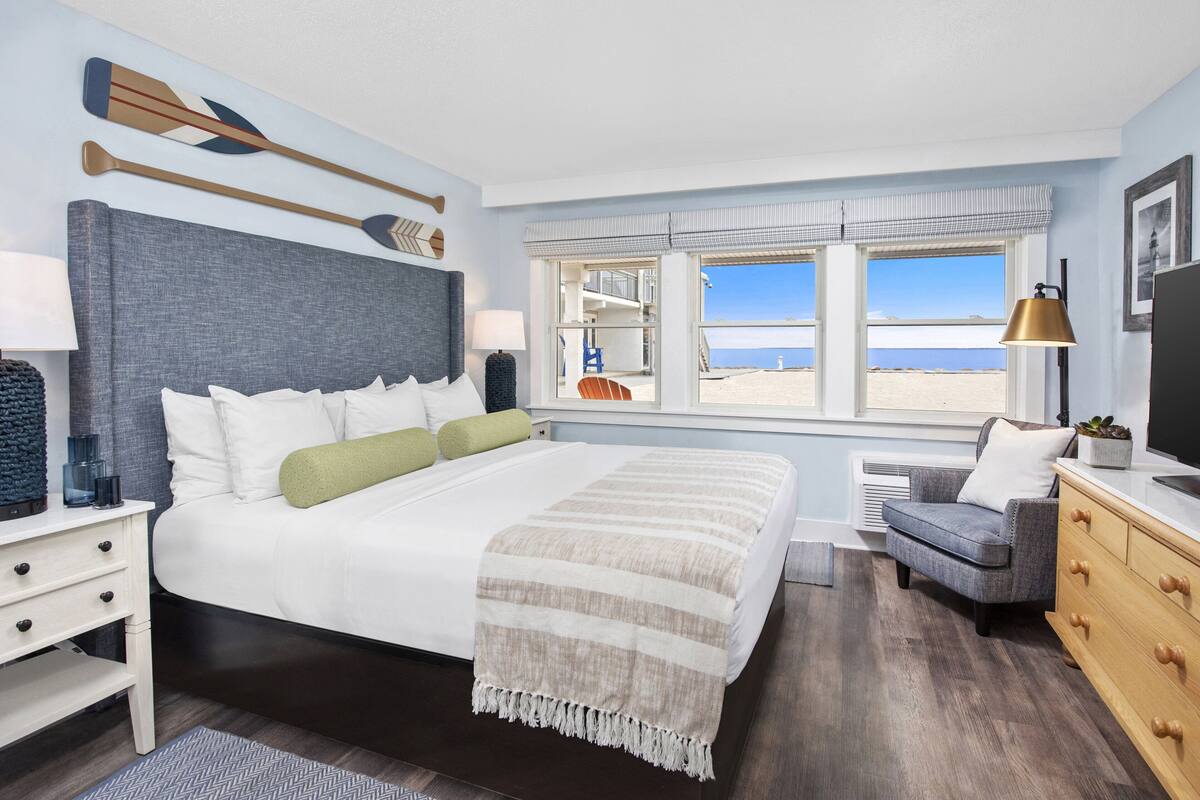 Ein Schlafzimmer mit einem großen Bett, Meerblick, einem Sessel und einer Kommode.