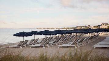 A beach with rows of sun loungers and umbrellas, a sandy shore, and a calm sea.