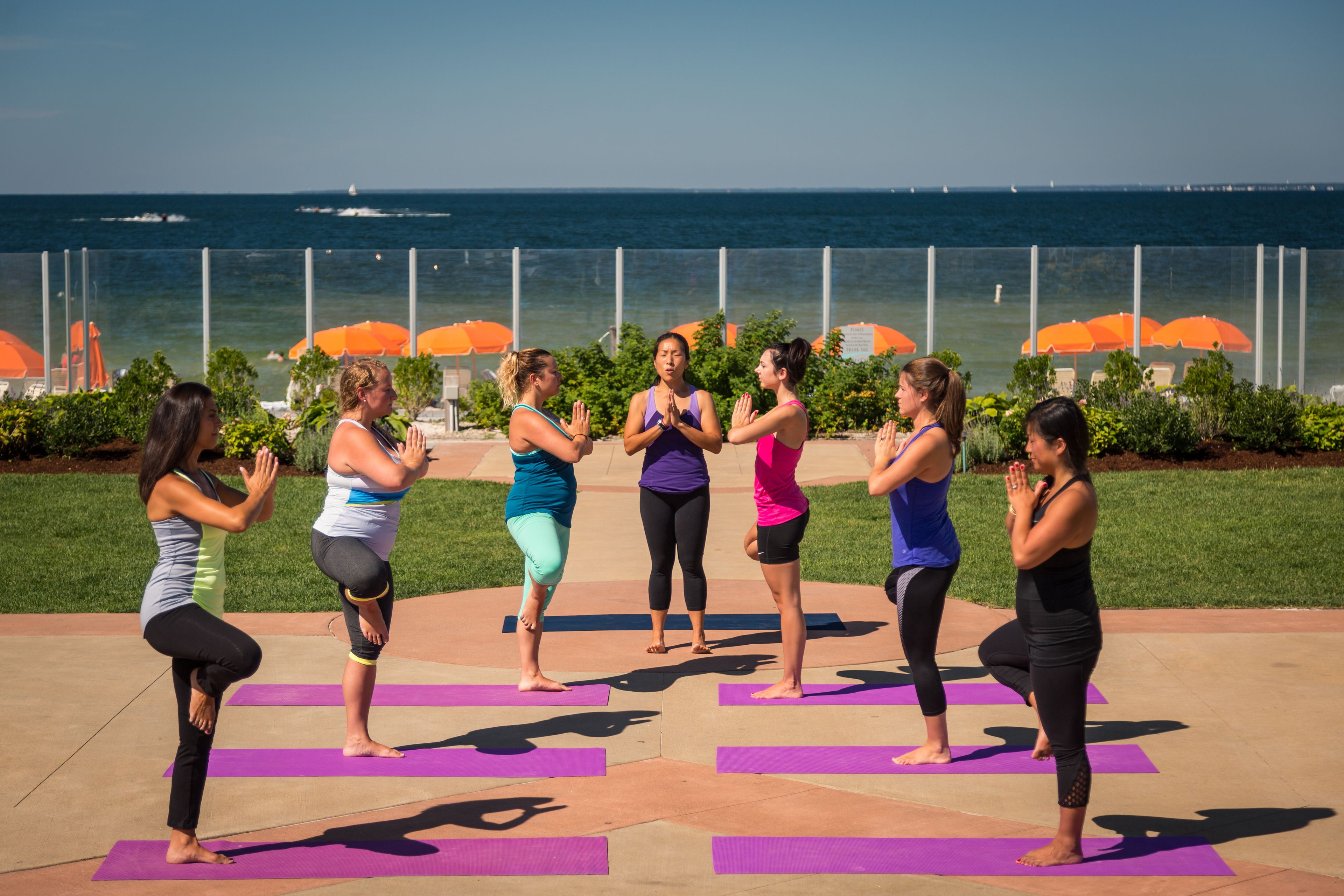A group of people performing yoga on mats in an outdoor setting with a view of the ocean.
