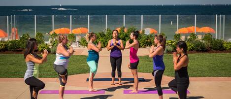 A group of people performing yoga on mats in an outdoor setting with a view of the ocean.