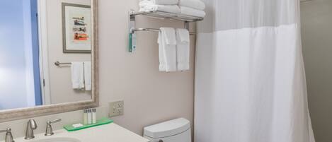 Un baño con un lavamanos blanco, inodoro, cortina de ducha y toallero.