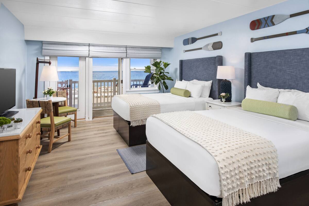 Ein Hotelzimmer mit zwei Betten, einem Schreibtisch mit Stuhl, einem Fernseher und Blick auf den Ozean.