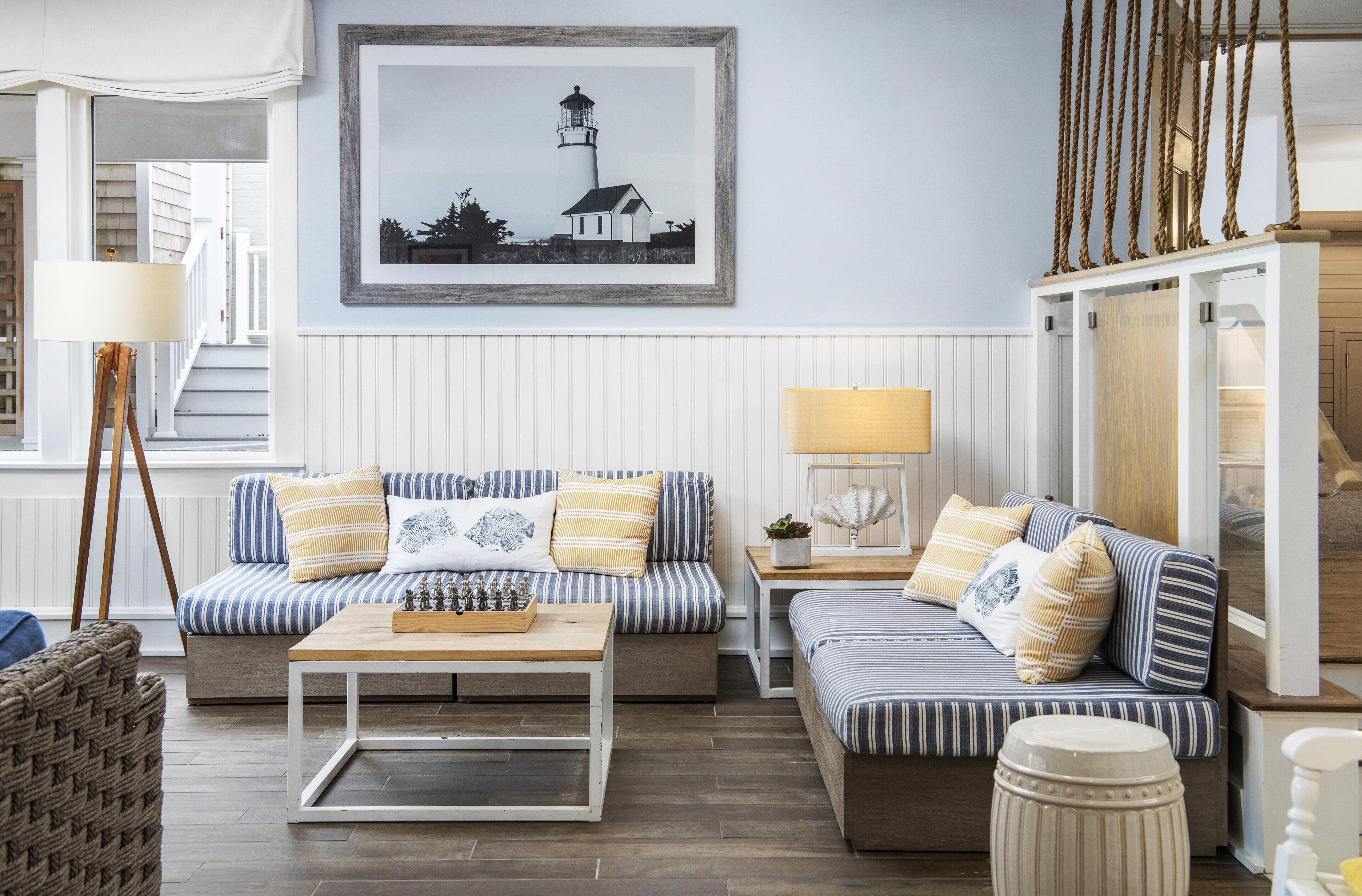Un salon chaleureux avec des canapés à rayures, une table basse et un tableau encadré représentant un phare.