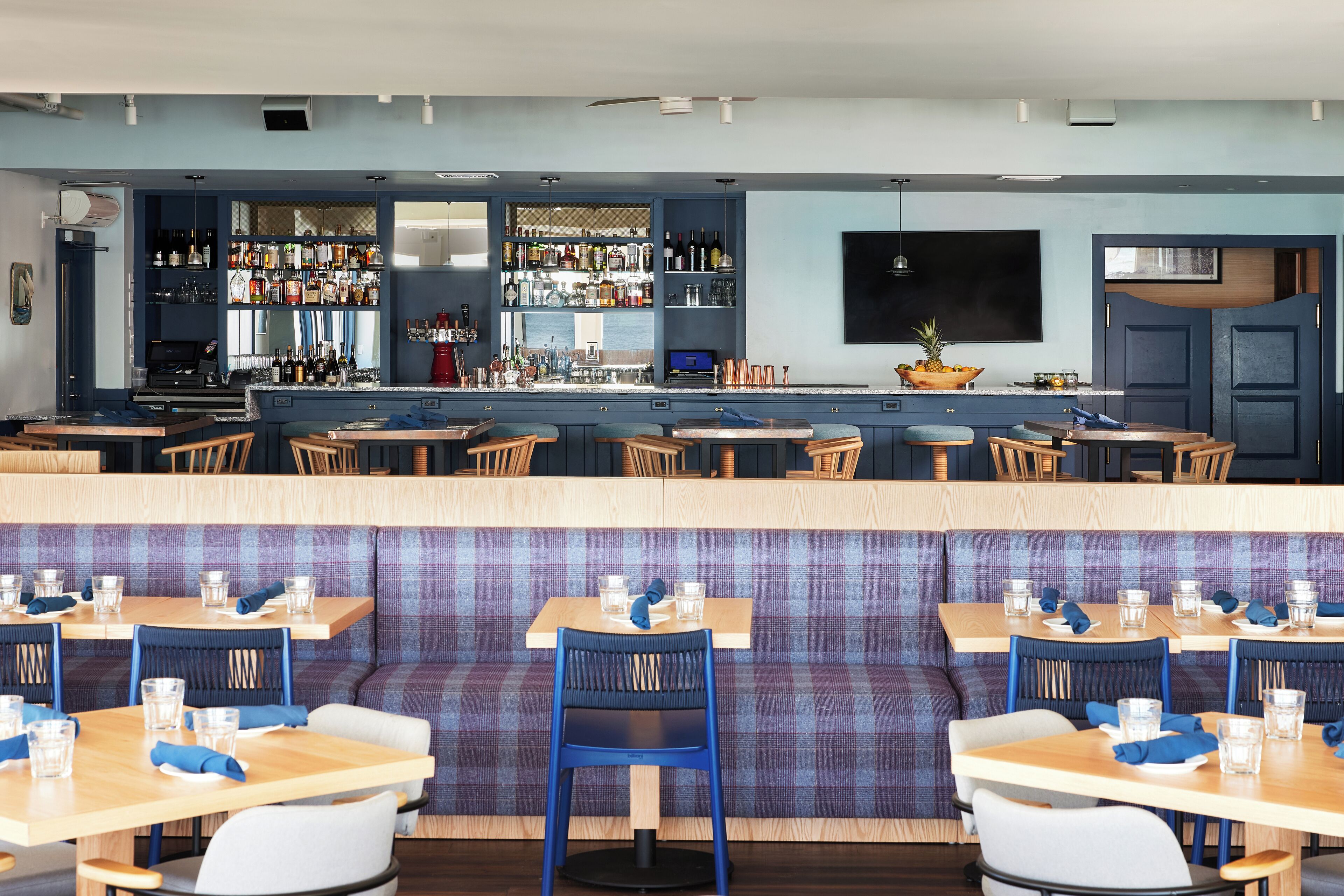 Een restaurant met een bar, zitplaatsen met tafels en stoelen, en diverse flessen en glazen op planken.