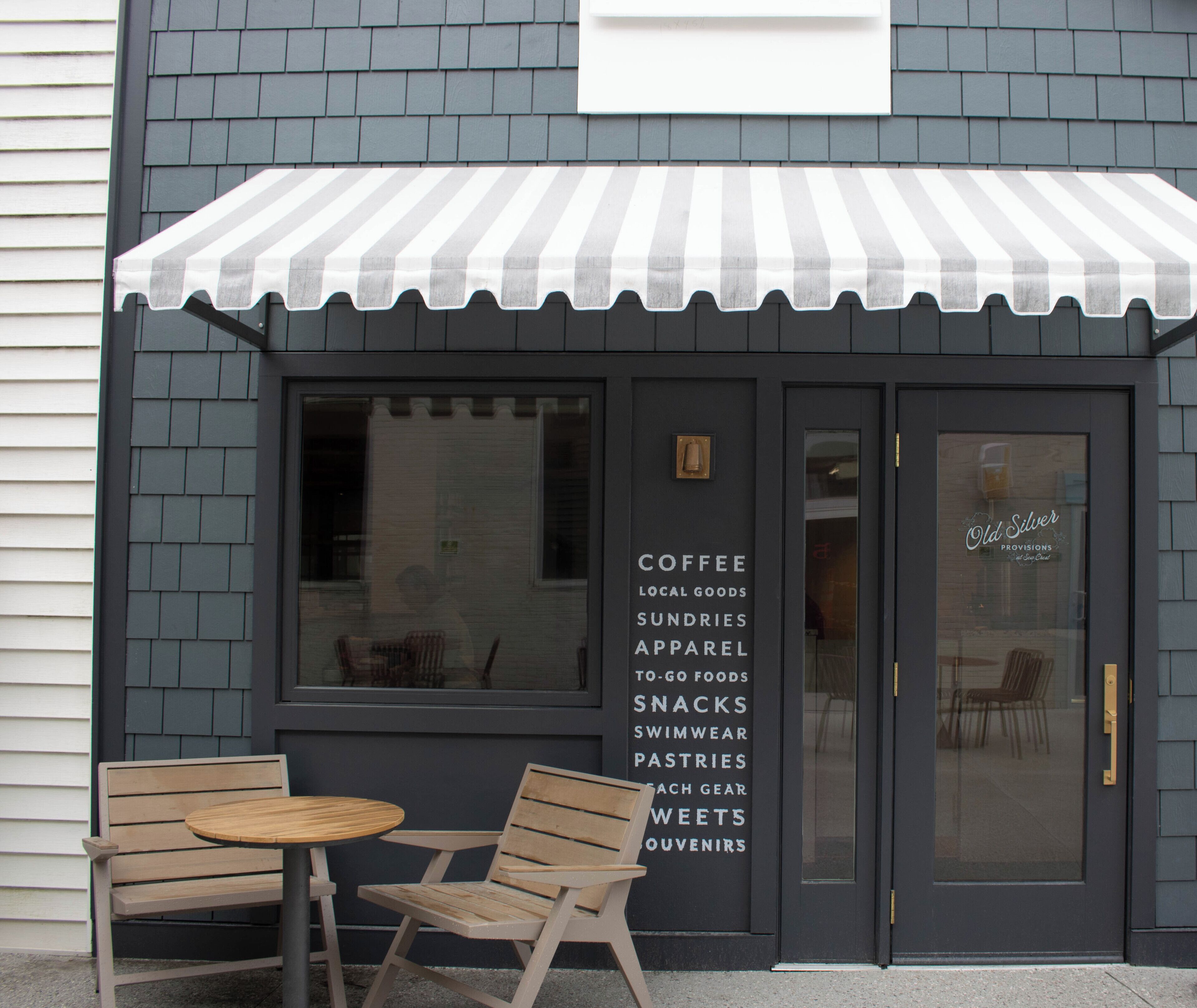 A storefront with a striped awning, a wooden bench, and a list of items including coffee, local goods, and apparel.