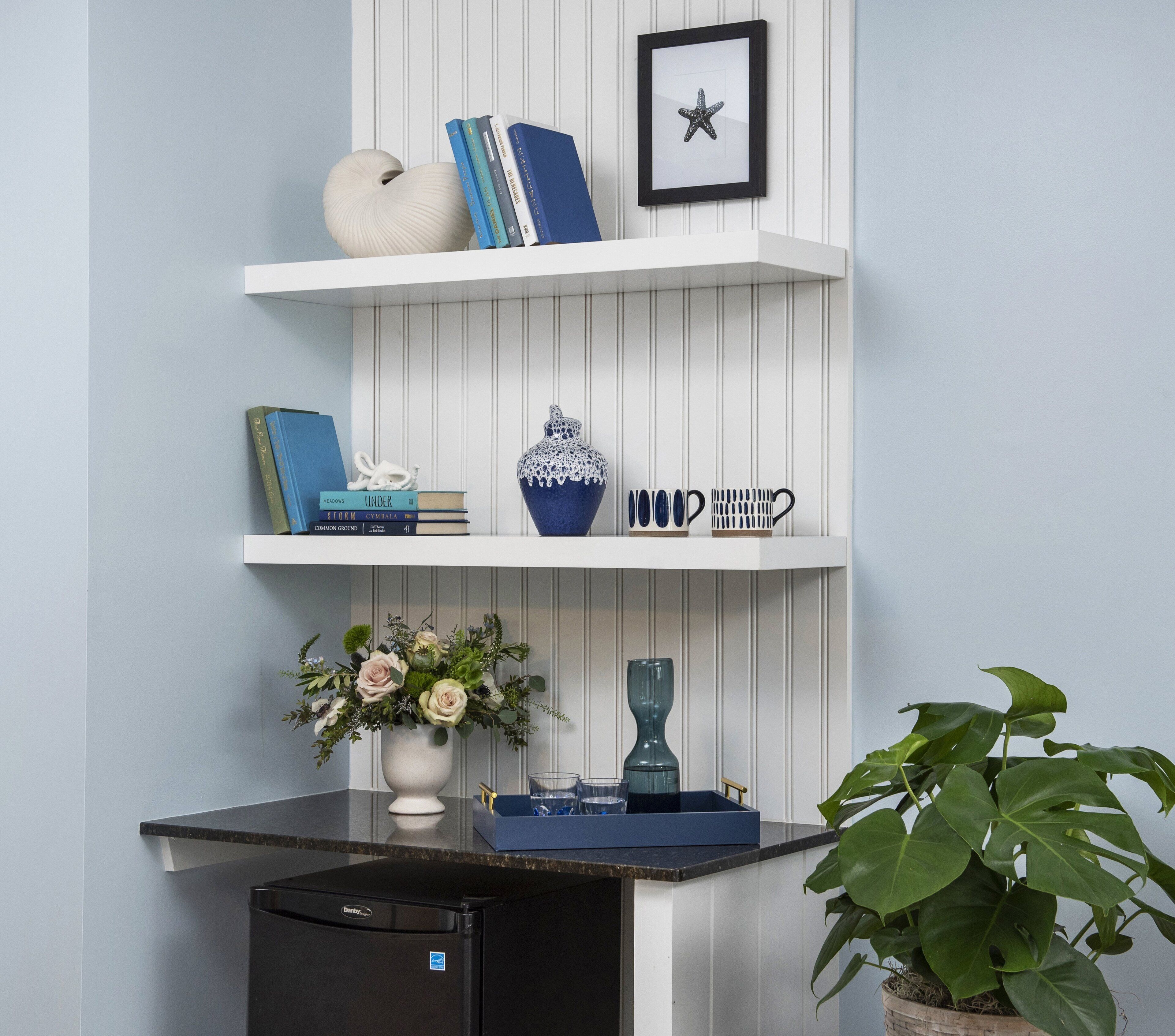 A kitchen with white shelves, a white vase with flowers, a blue vase, and a potted plant.