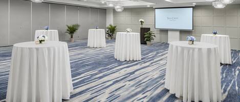 Ein Konferenzraum mit runden Tischen, einer Projektionsleinwand und einem Teppichboden.