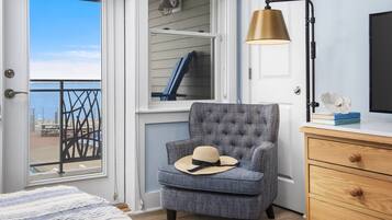 Ein Zimmer mit Meerblick, ein Sessel mit Hut, eine Lampe und eine Holzkommode.