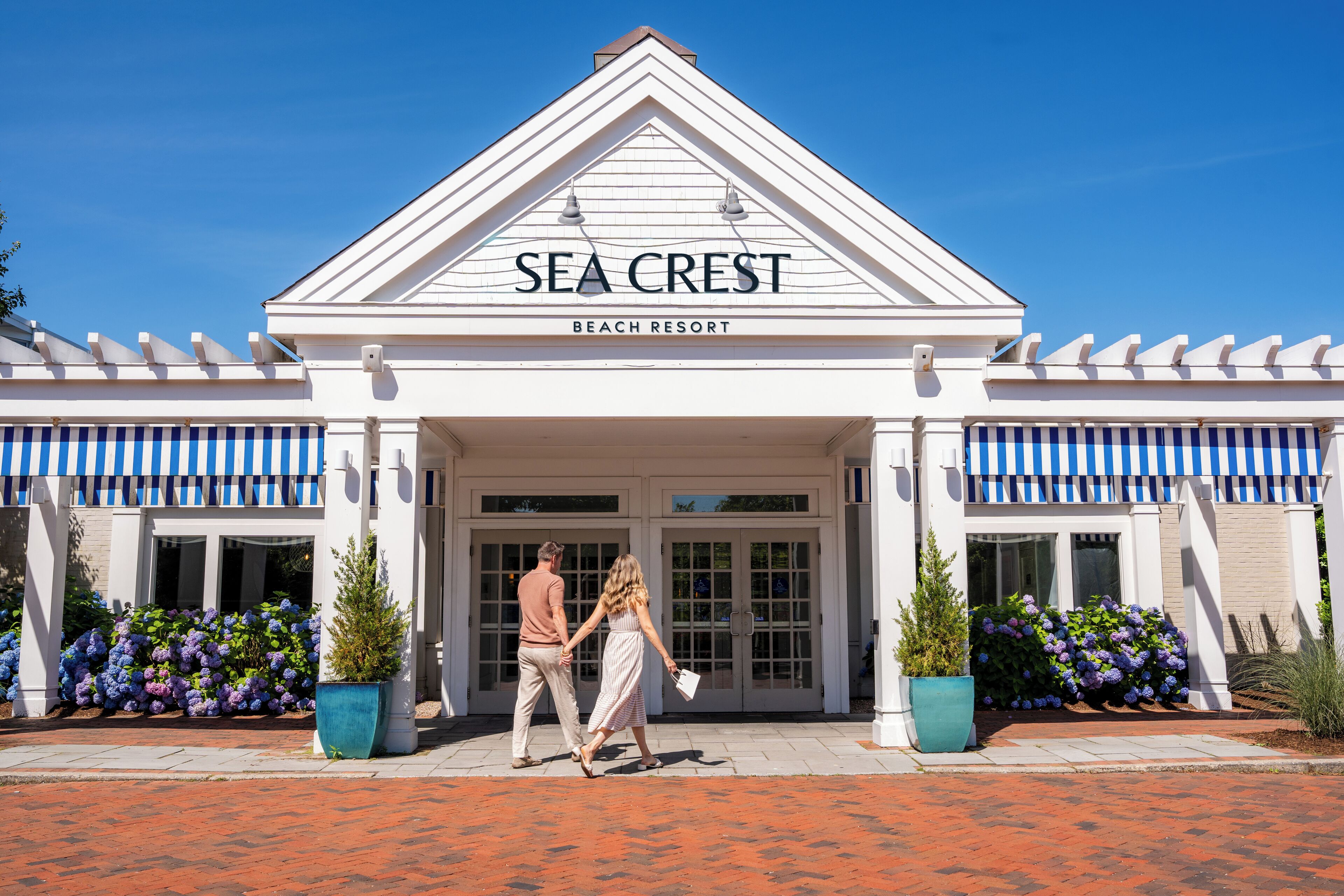 A beach resort named Sea Crest with a white facade, blue-striped awnings, and potted plants.