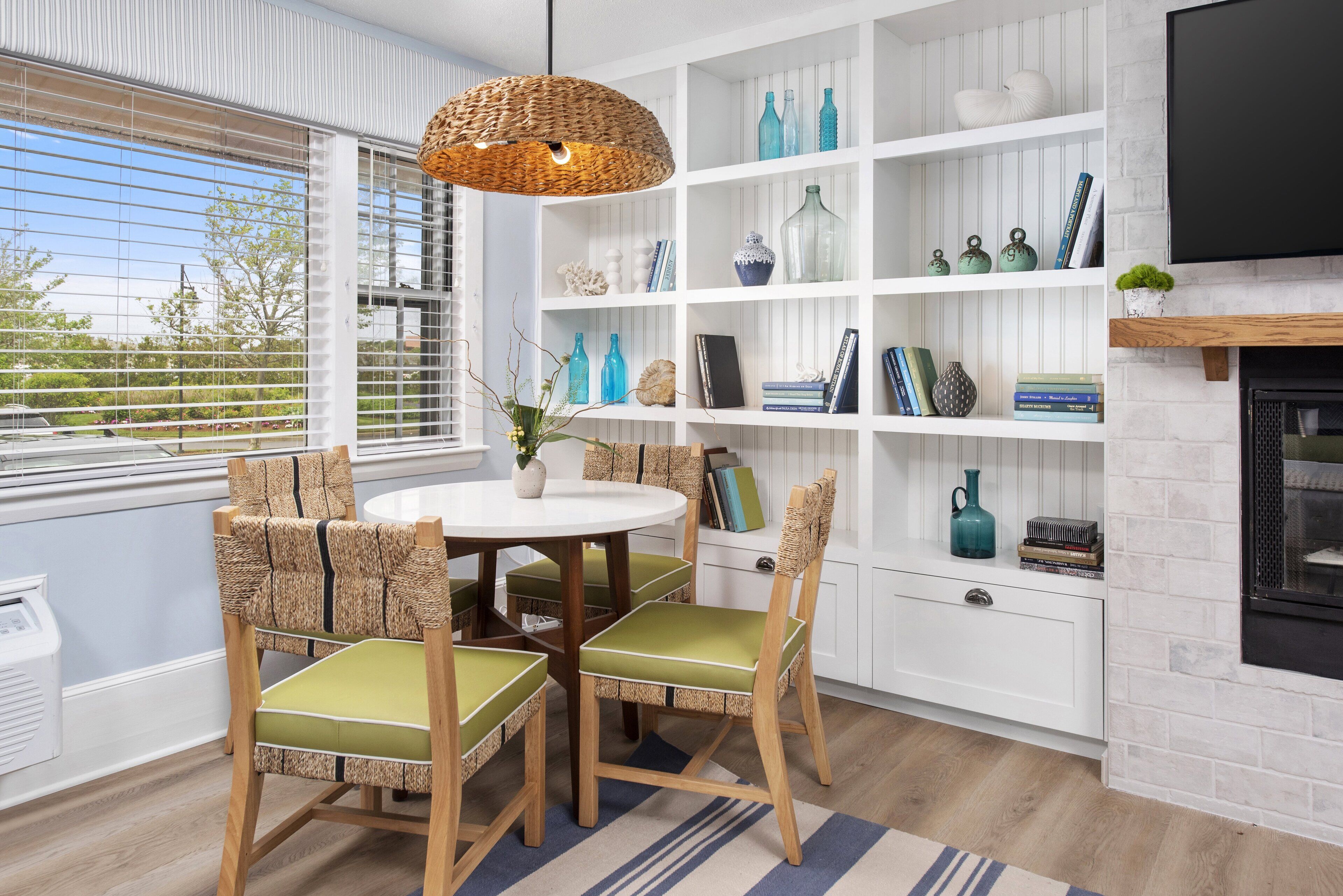 A dining area with a round table and chairs, a white shelving unit with decorative items, and a fireplace.