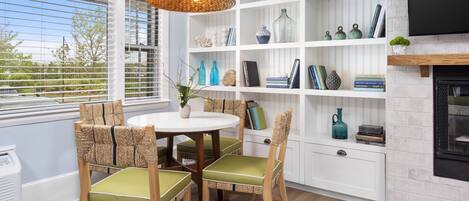 A dining area with a round table and chairs, a white shelving unit with decorative items, and a fireplace.
